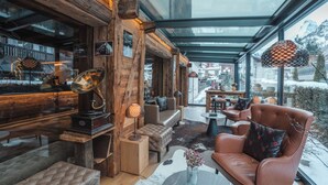 A modern interior with wooden accents, a leather sofa, a glass ceiling, and a view of the outside. - Zermatt Budget Rooms at Alpen Resort, Spa & Dining (Zermatt)