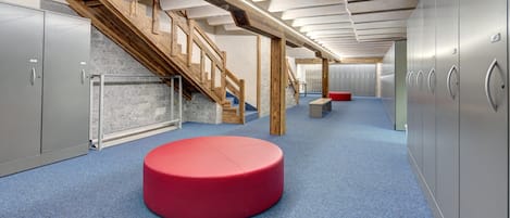 Un interior moderno con una escalera, taquillas y una zona de estar circular roja.