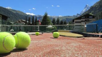 Una cancha de tenis con una red, rodeada de edificios y montañas.