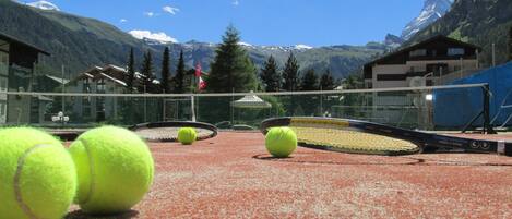 A tennis court with a net, surrounded by buildings and mountains.