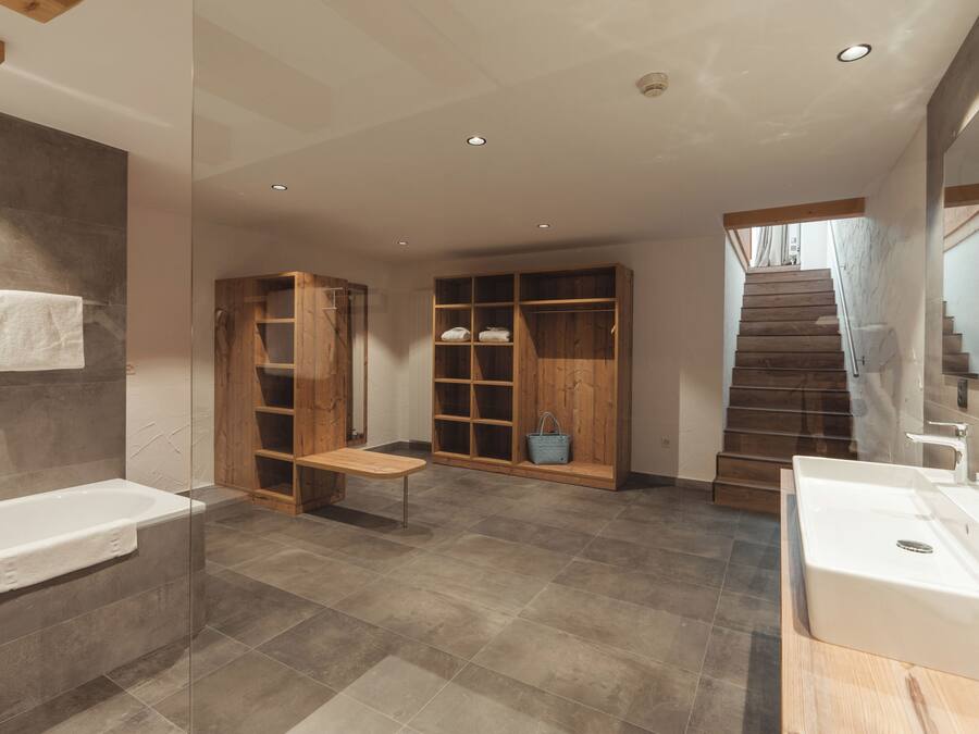 Un bagno moderno con una vasca, una panca in legno, un mobile lavabo e una scala che conduce a un livello superiore.