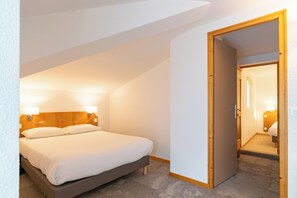A bedroom with a bed, bedside lamps, and a wooden door leading to another room. - Hotel beau site (Malbuisson)