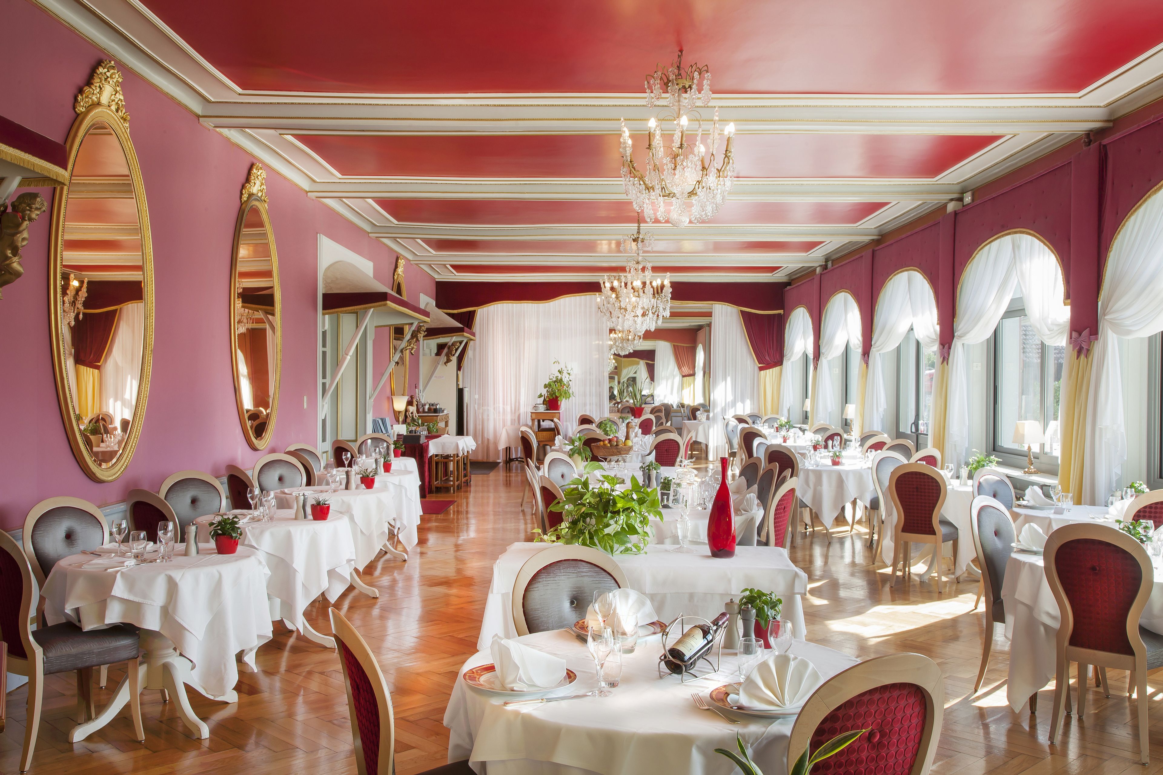 A formal dining room with tables set for service, elegant chandeliers, and large mirrors on the walls.