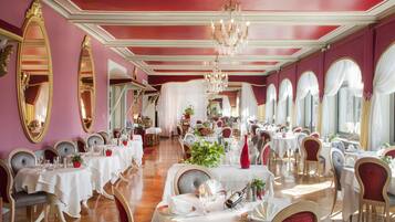 A formal dining room with tables set for service, elegant chandeliers, and large mirrors on the walls.