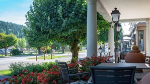 An outdoor seating area with tables and chairs, surrounded by greenery and flowers. - Hotel beau site (Malbuisson)