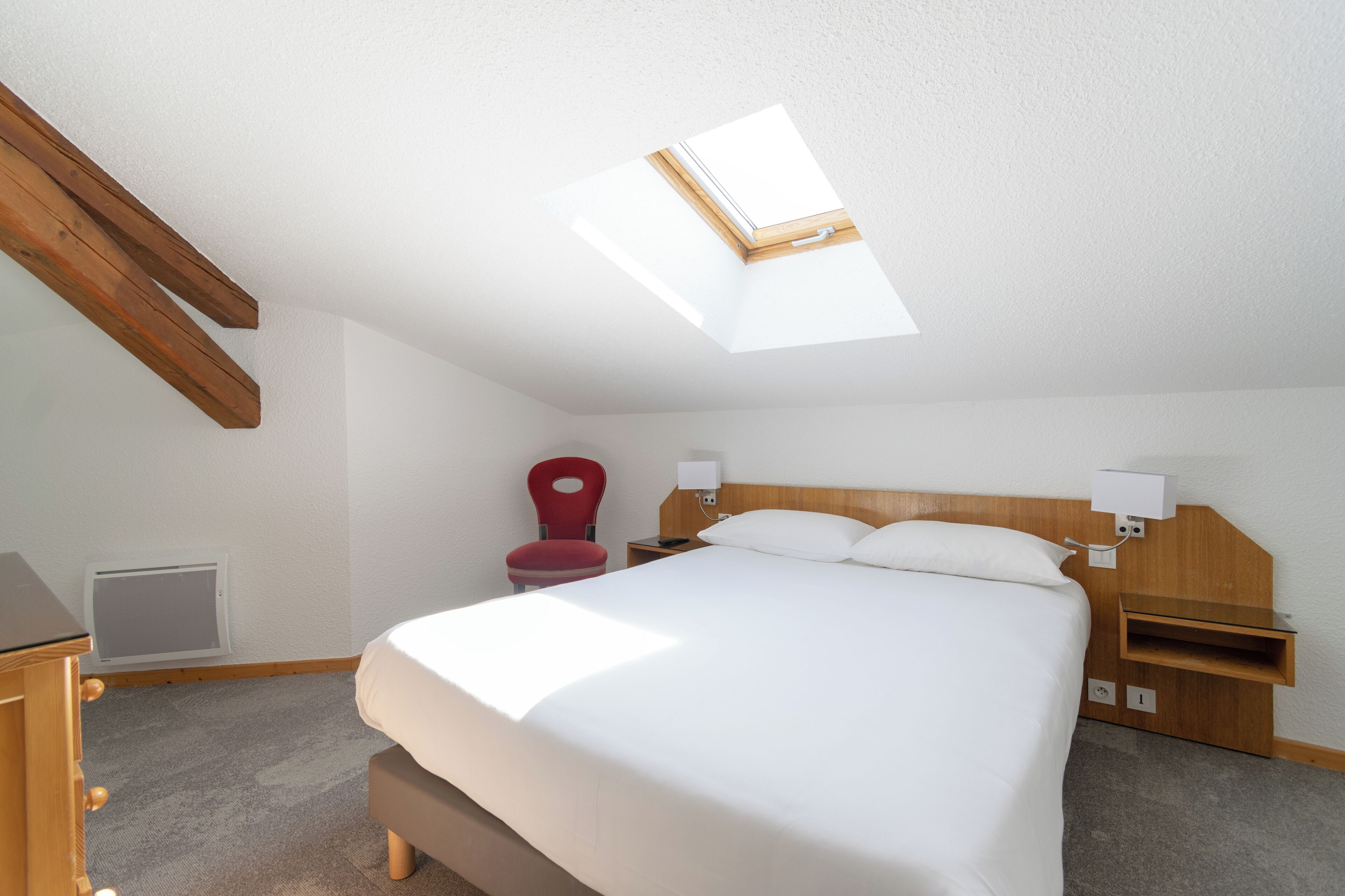 Un dormitorio con tragaluz, una cama, una mesita de noche, una silla y un aparador de madera.