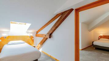 A bedroom with a sloped ceiling, wooden beams, a bed, bedside tables, and wall-mounted lamps.
