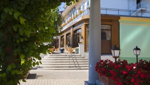 A hotel entrance with a staircase leading to a balcony, a flower bed, and a lamp post. - Hotel beau site (Malbuisson)