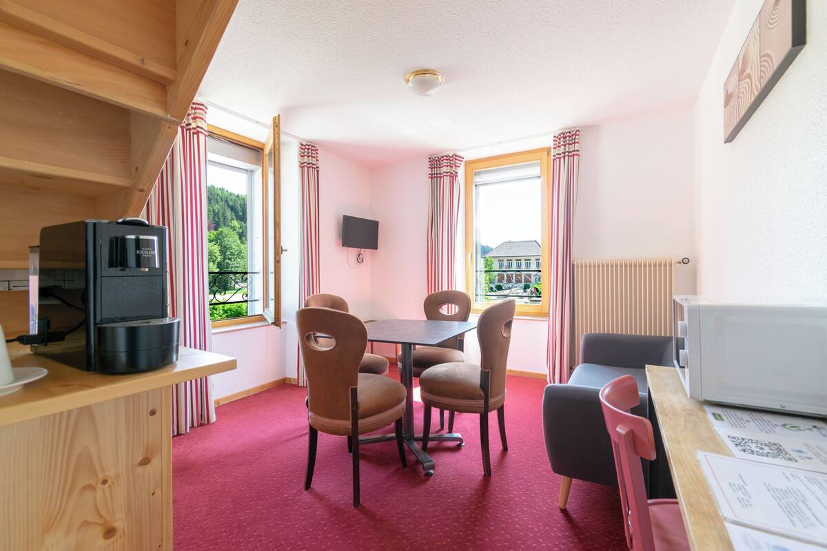 A cozy room with a wooden table, chairs, a television, a microwave, and a window with curtains.