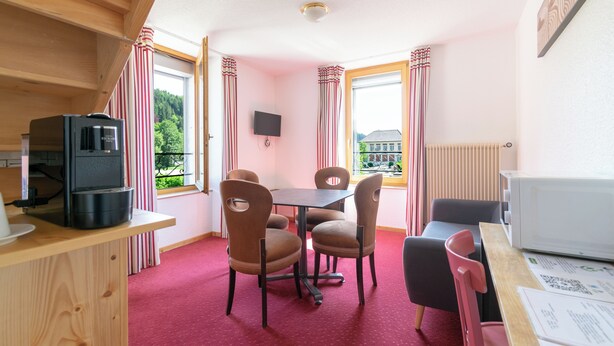Una habitación acogedora con una mesa de madera, sillas, un televisor, un microondas y una ventana con cortinas.