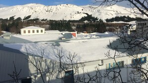 A snow-covered landscape with buildings, including a large industrial facility with a flat roof and a smaller structure with a red roof. - Hot Springs Hostel (Hveragerdi)