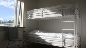 A bunk bed with a chair in a room with a window. - Hot Springs Hostel (Hveragerdi)