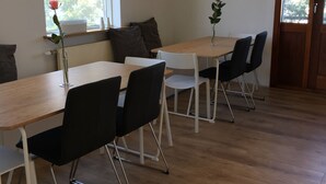 A dining area with wooden tables and chairs, two pendant lights, and a window with a view of trees. - Hot Springs Hostel (Hveragerdi)