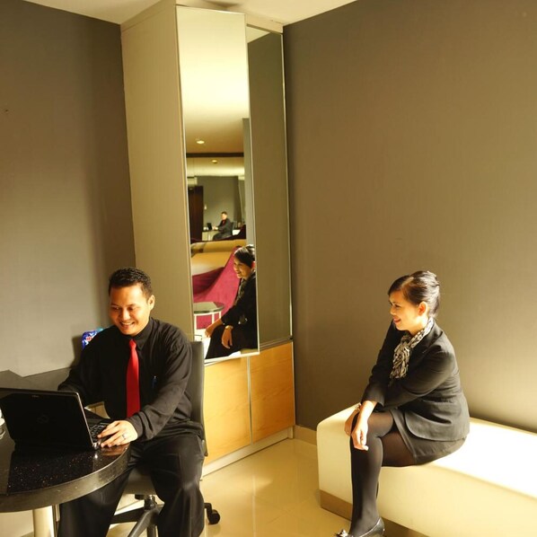 A modern hotel room with a large mirror, a laptop on a table, and a person sitting on a bench. - B Fashion Hotel (Jakarta)