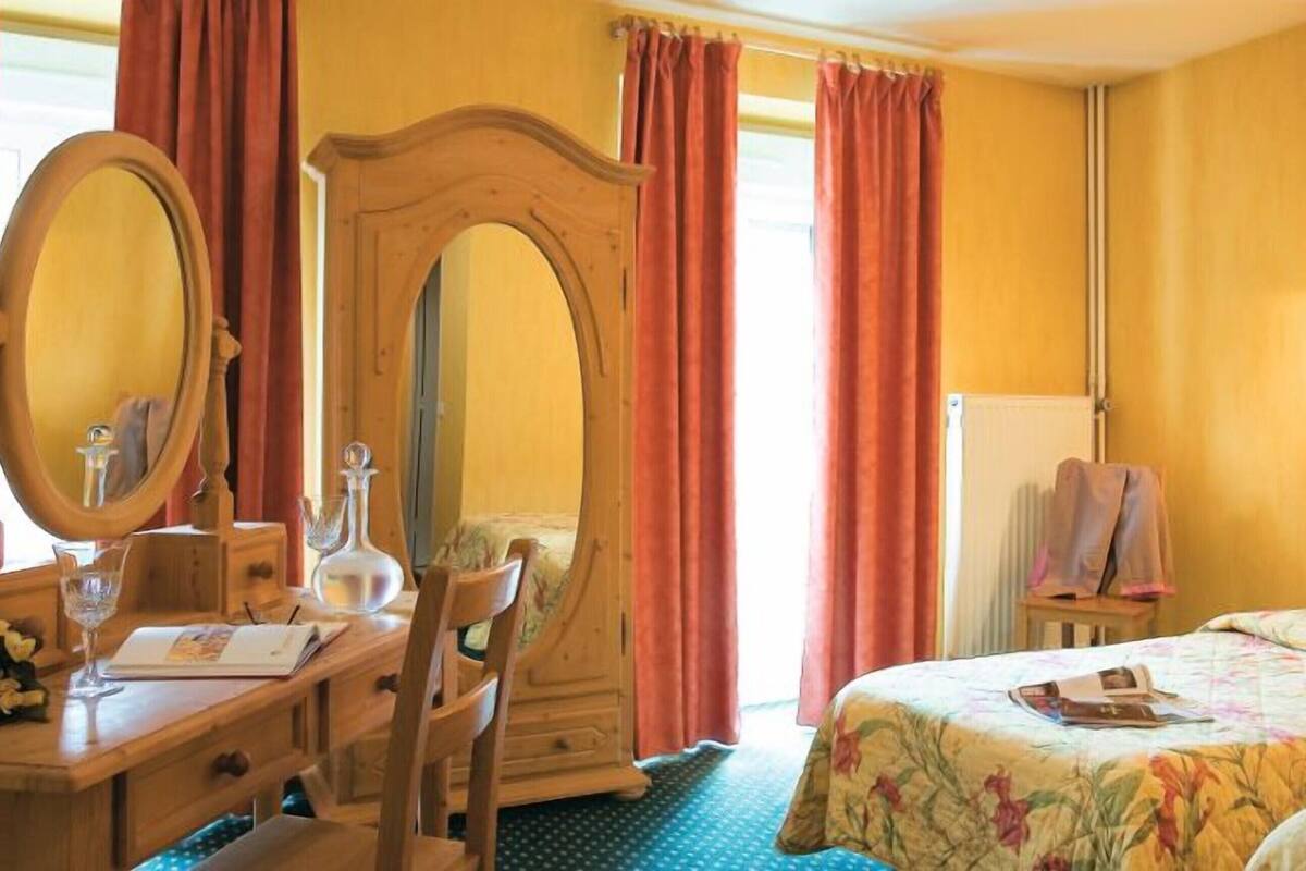 A hotel room with a wooden desk, a large mirror, two beds with floral bedding, and a rooster decoration.