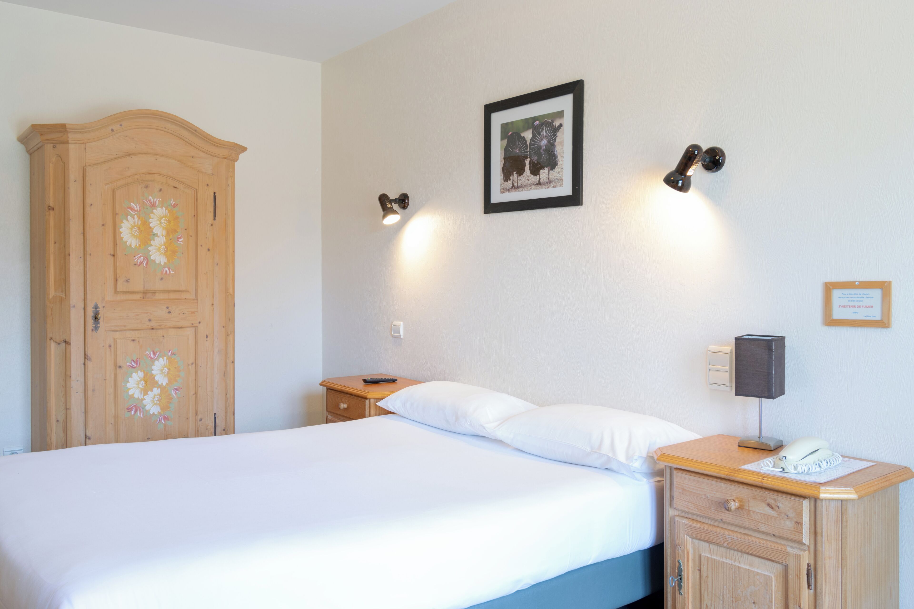 Un dormitorio con cama, armario de madera, mesita de noche con lámpara y un cuadro enmarcado en la pared.