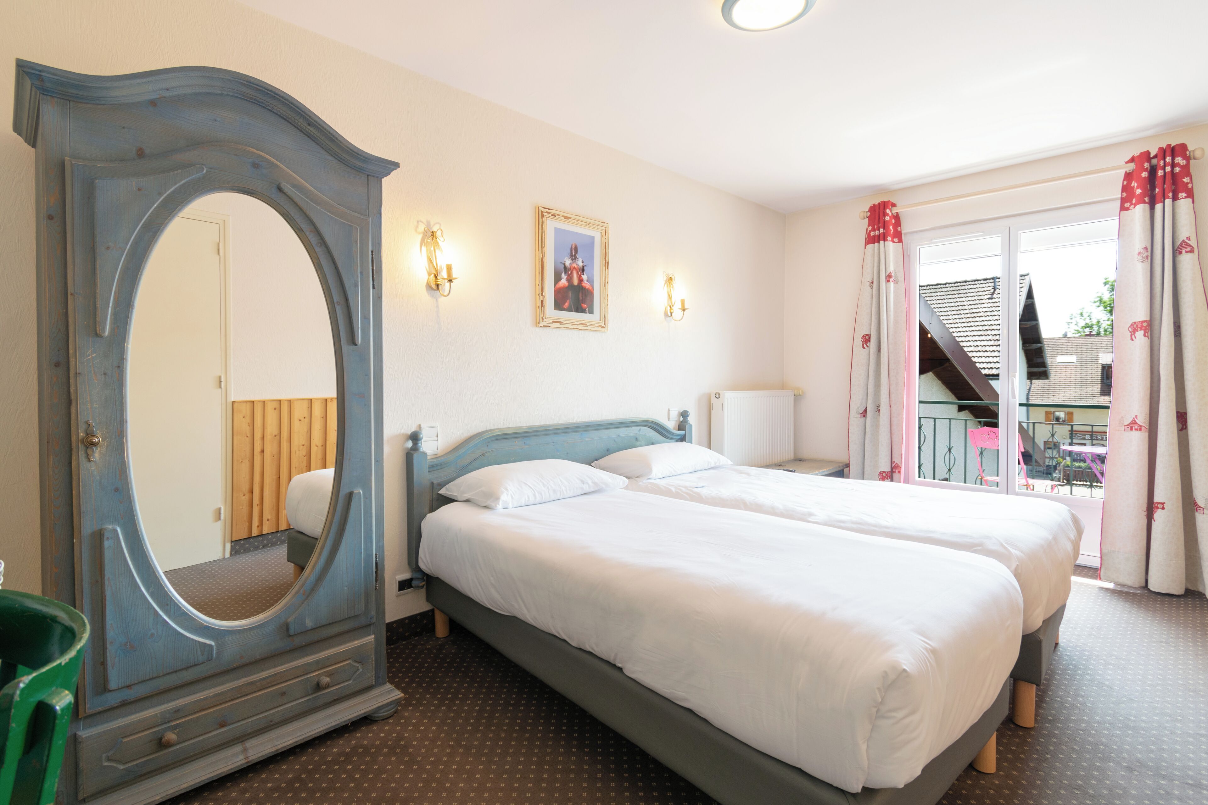 A hotel room with two beds, a large mirror, wall sconces, and a view of the outside balcony.