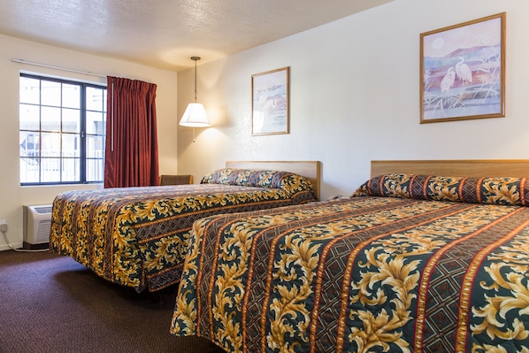 Habitación de hotel con dos camas, un ventanal con cortinas, una lámpara fijada a la pared y dos cuadros enmarcados.