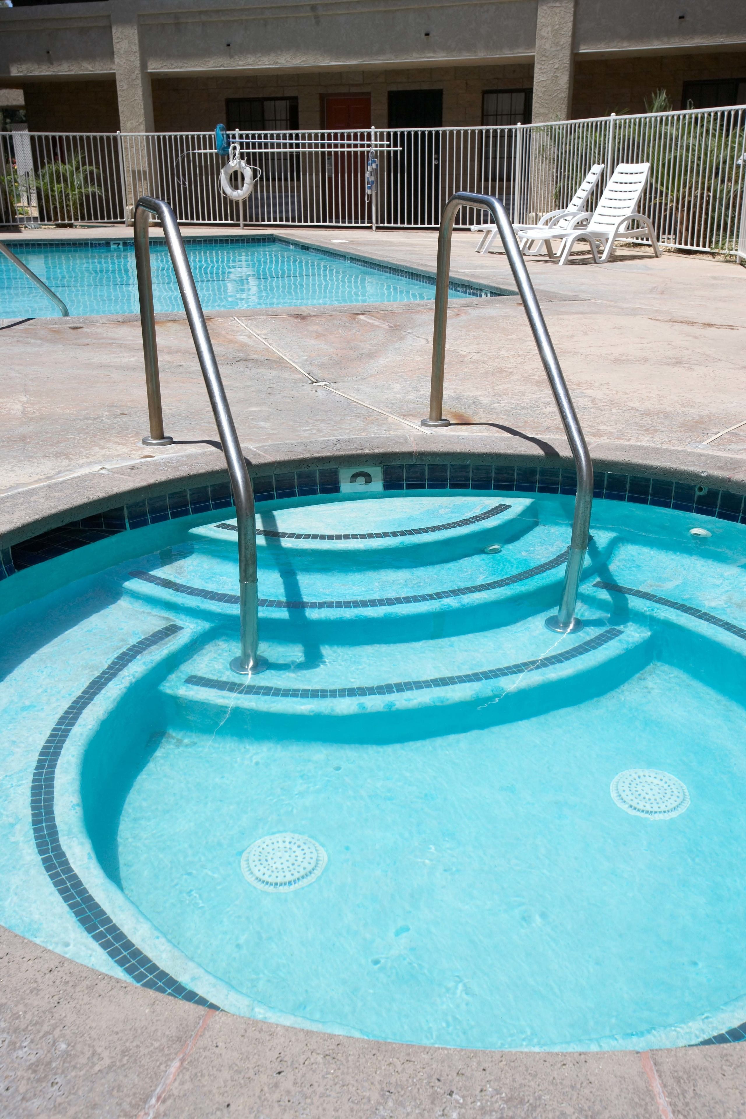 A swimming pool with metal ladders, tiled steps, and lounge chairs in the background.