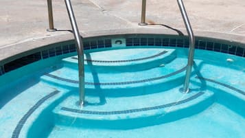 A swimming pool with metal ladders, tiled steps, and lounge chairs in the background.