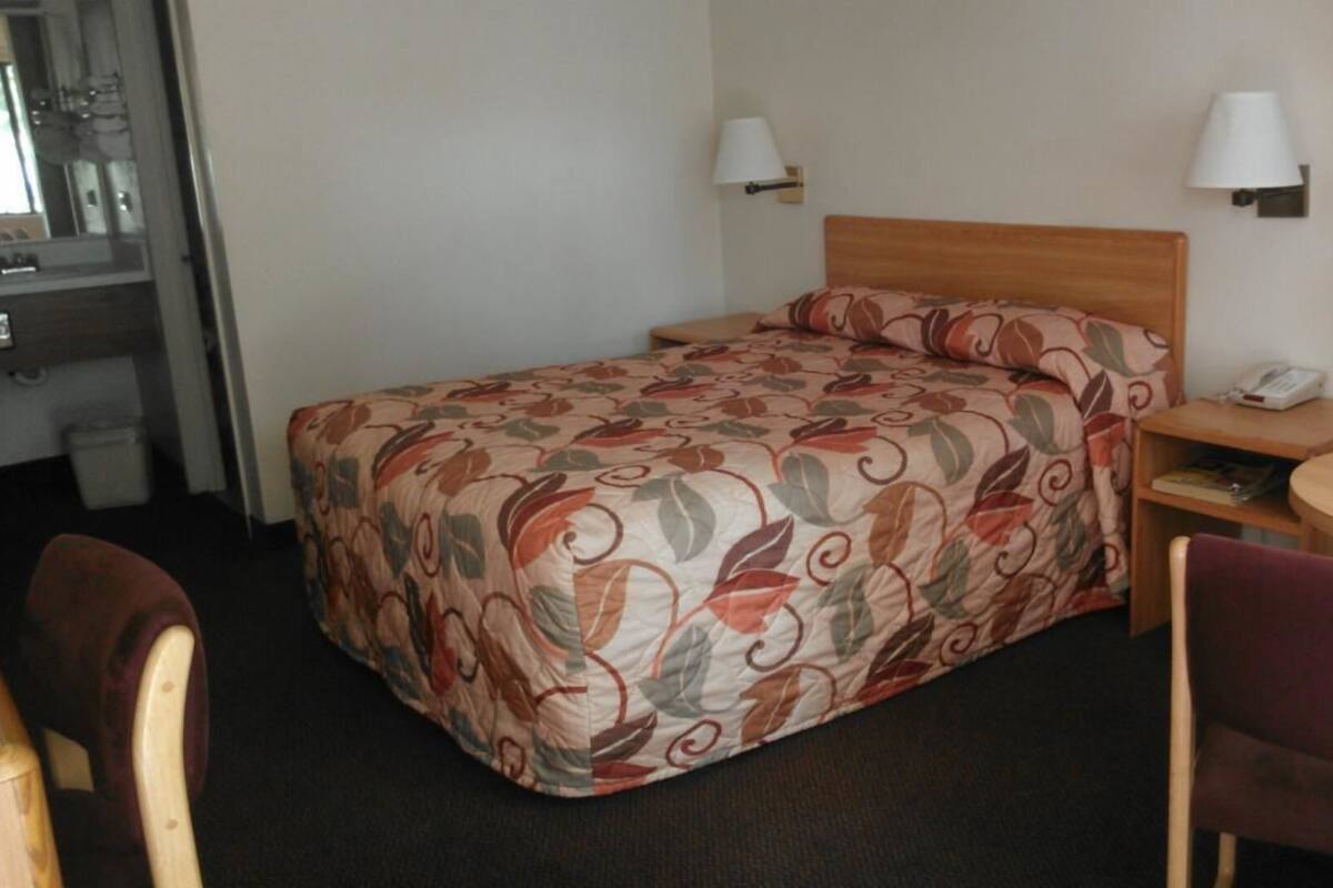 A hotel room with a bed, two bedside lamps, a small table with a remote control, a chair, and a desk with a telephone.