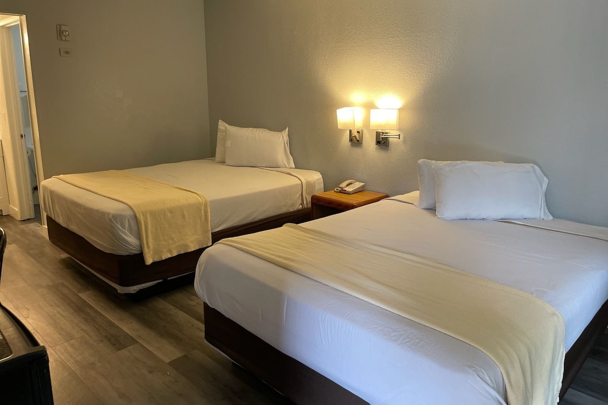 A hotel room with two beds, a wooden floor, and a nightstand with a phone.