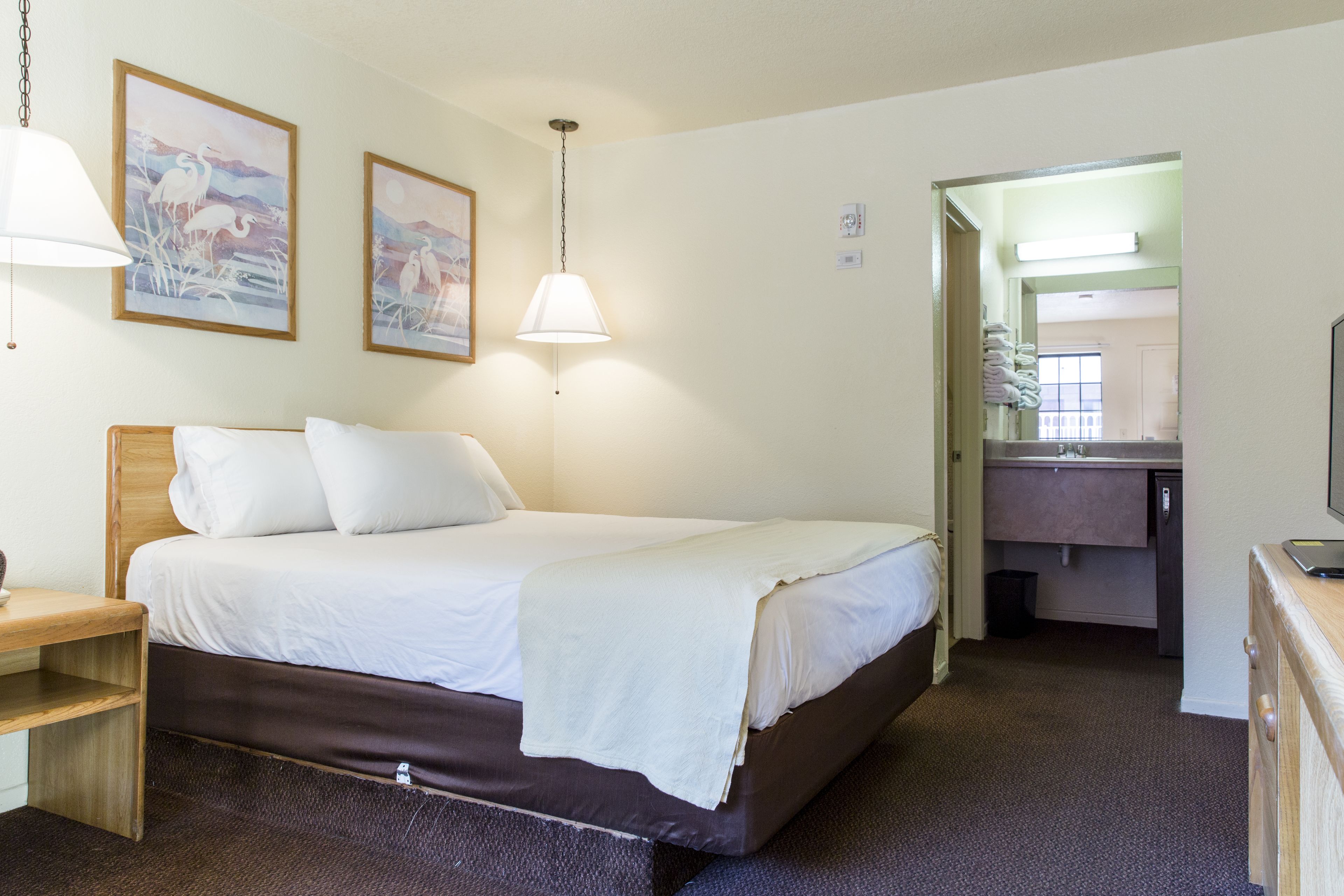 A hotel room with a bed, bedside table, lamp, and artwork on the wall.