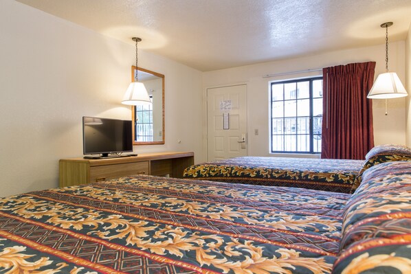 A hotel room with two beds, a TV on a wooden dresser, a window with curtains, and a hanging lamp.