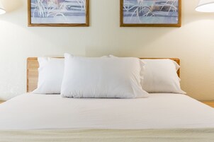 Una cama bien tendida con sábanas y almohadas blancas, enmarcada por un cabecero de madera.