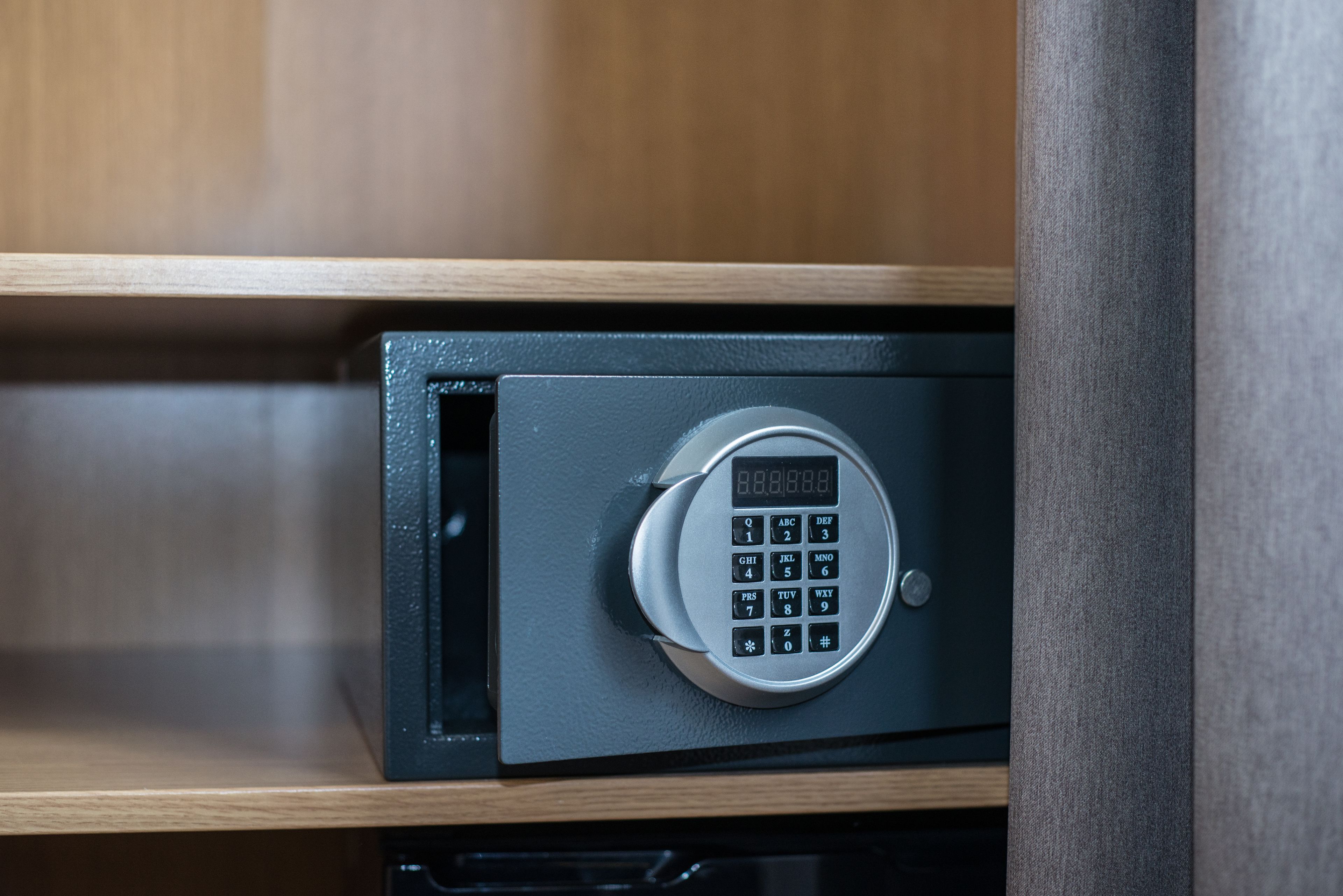 A black safe with a keypad on a wooden shelf.