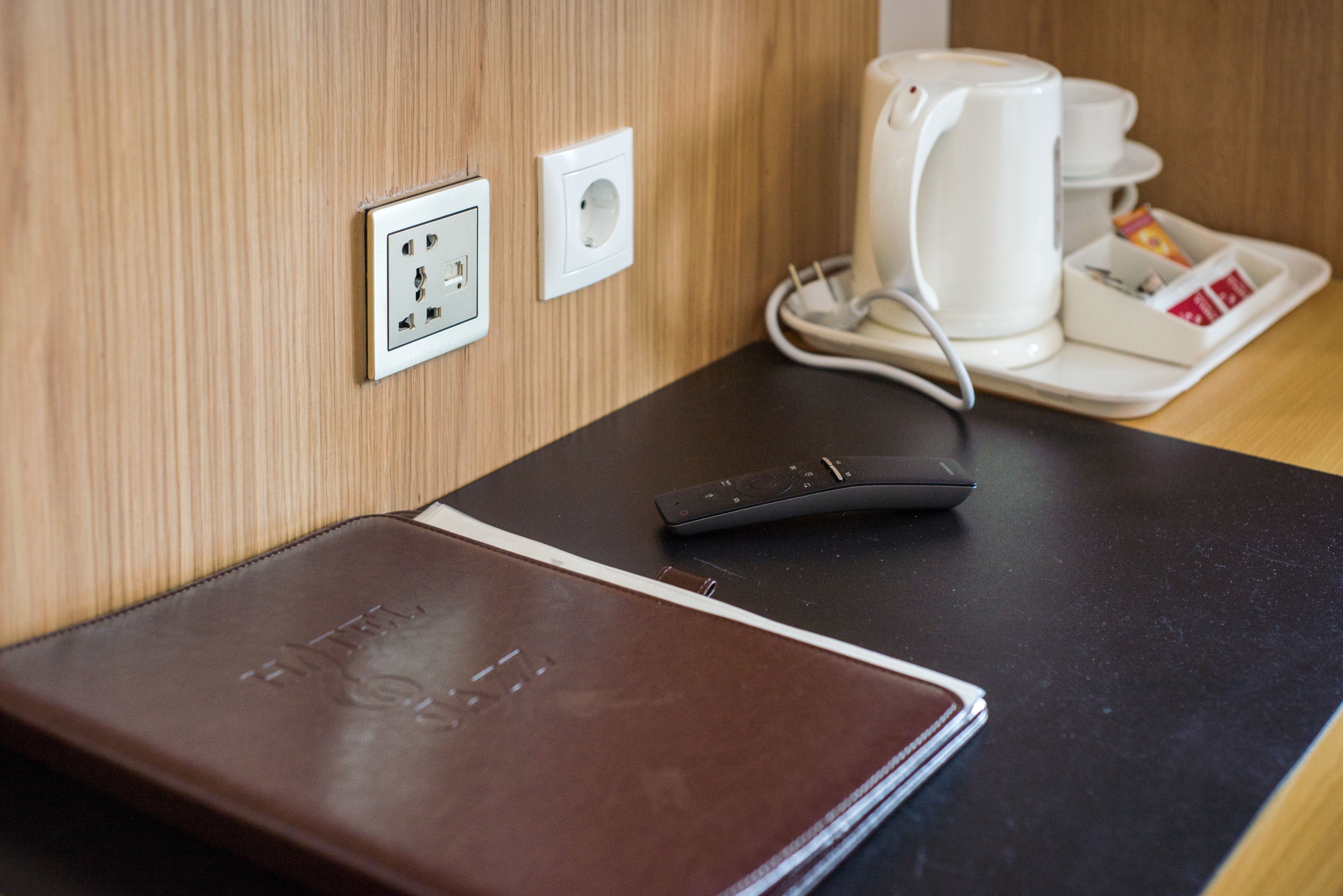 Una habitación de hotel con una carpeta de cuero marrón, una cafetera blanca y un control remoto sobre una mesa negra.