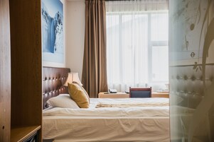 Una habitación de hotel con cama, mesita de noche, lámpara, un cuadro y una ventana con cortinas.