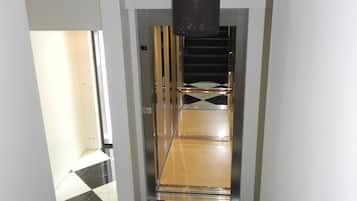 A hallway with a checkered floor, an emergency exit sign, and a staircase leading to an elevator.