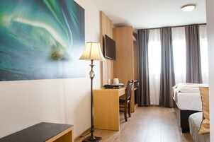 Habitación de hotel con escritorio, silla, cama, televisión y un cuadro de la aurora boreal.
