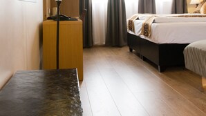 Habitación de hotel con cama, mesita de noche con lámpara, mesita auxiliar de madera y un cuadro en la pared.