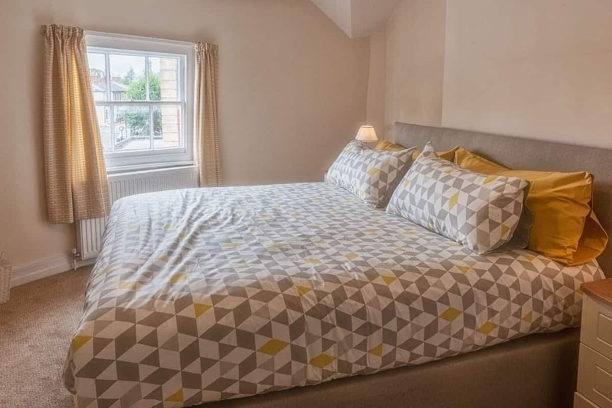 Quarto com uma cama, duas luminárias de cabeceira e janela com cortinas.