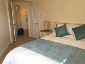 A bedroom with a bed, a nightstand, a lamp, and a door leading to a bathroom. - Luxury Town Centre Apartment Stratford Upon Avon (Stratford-upon-Avon)