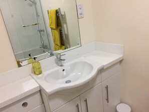 A bathroom with a white sink, a mirror, and a yellow towel hanging on a rack. - Luxury Town Centre Apartment Stratford Upon Avon (Stratford-upon-Avon)