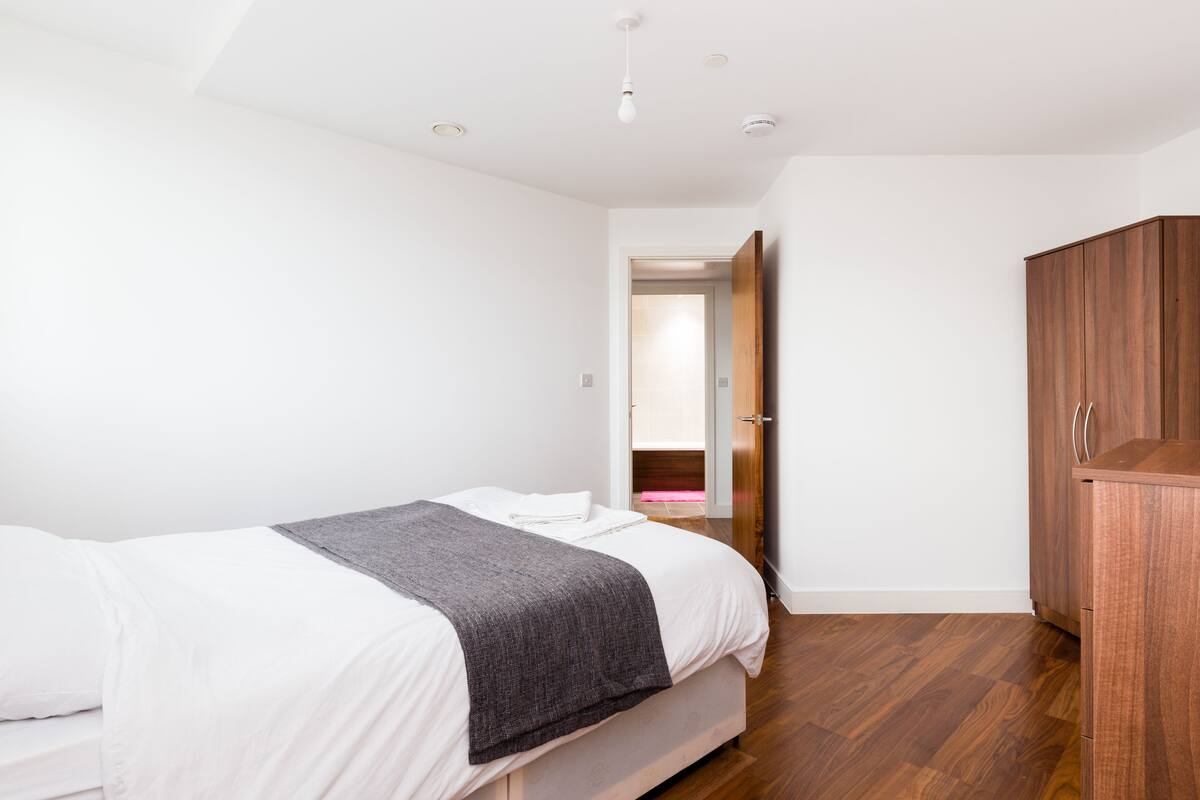 A bedroom with a bed, a wooden wardrobe, and a door leading to another room.