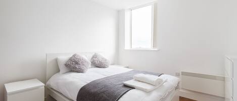 Un dormitorio ordenado con cama, mesitas de noche, un radiador y una ventana.