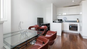 A modern kitchen with white cabinets, a built-in oven, and a dining area with a glass table and red chairs. - Birmingham Serviced Apartments Hagley Rd (Birmingham)