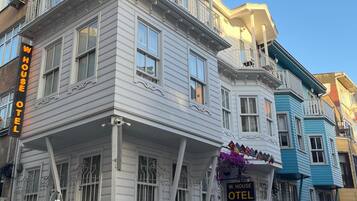 A multi-story building with a balcony, a sign reading "W.HOUSE HOTEL," and a staircase leading to the entrance.