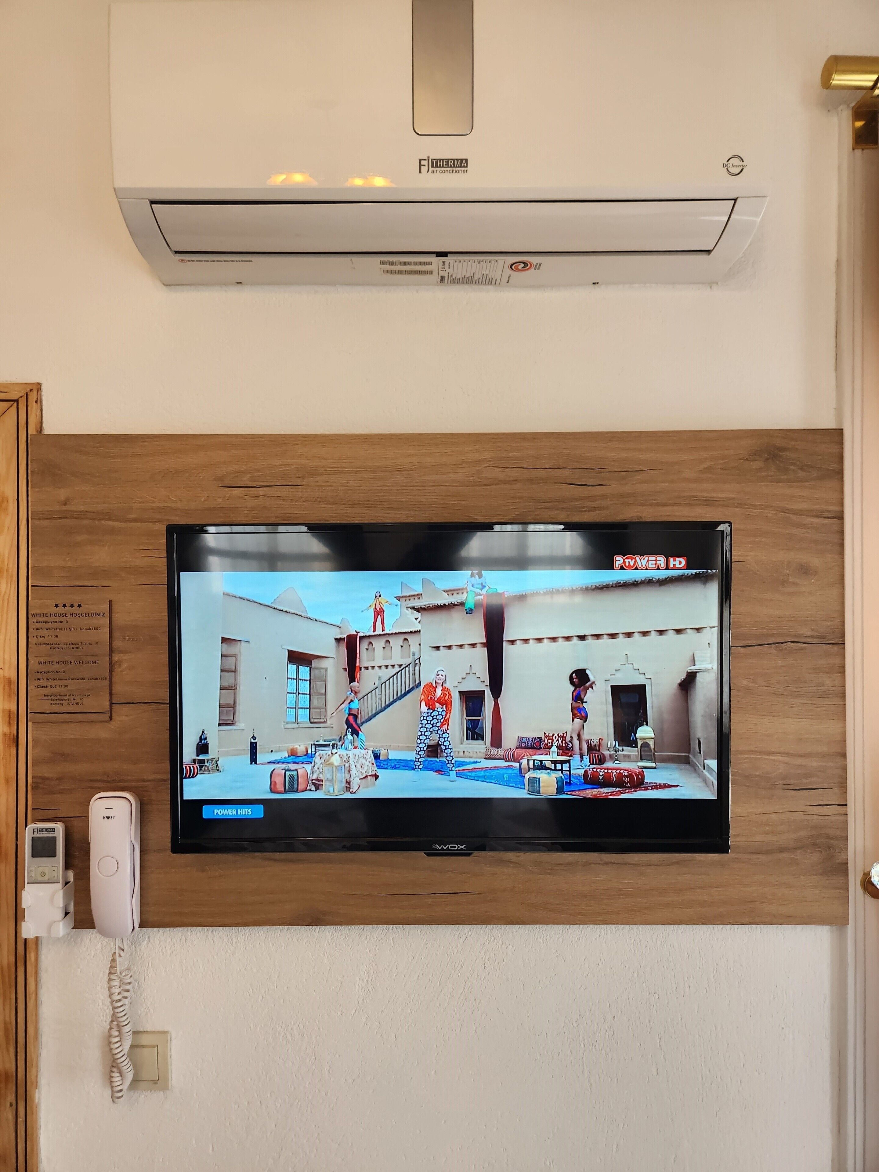 Ein Flachbildfernseher an einer Holzwand montiert, zeigt eine Szene aus 'Power Hits'.