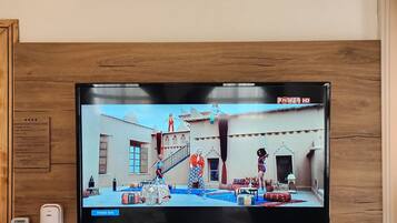 Ein Flachbildfernseher an einer Holzwand montiert, zeigt eine Szene aus 'Power Hits'.