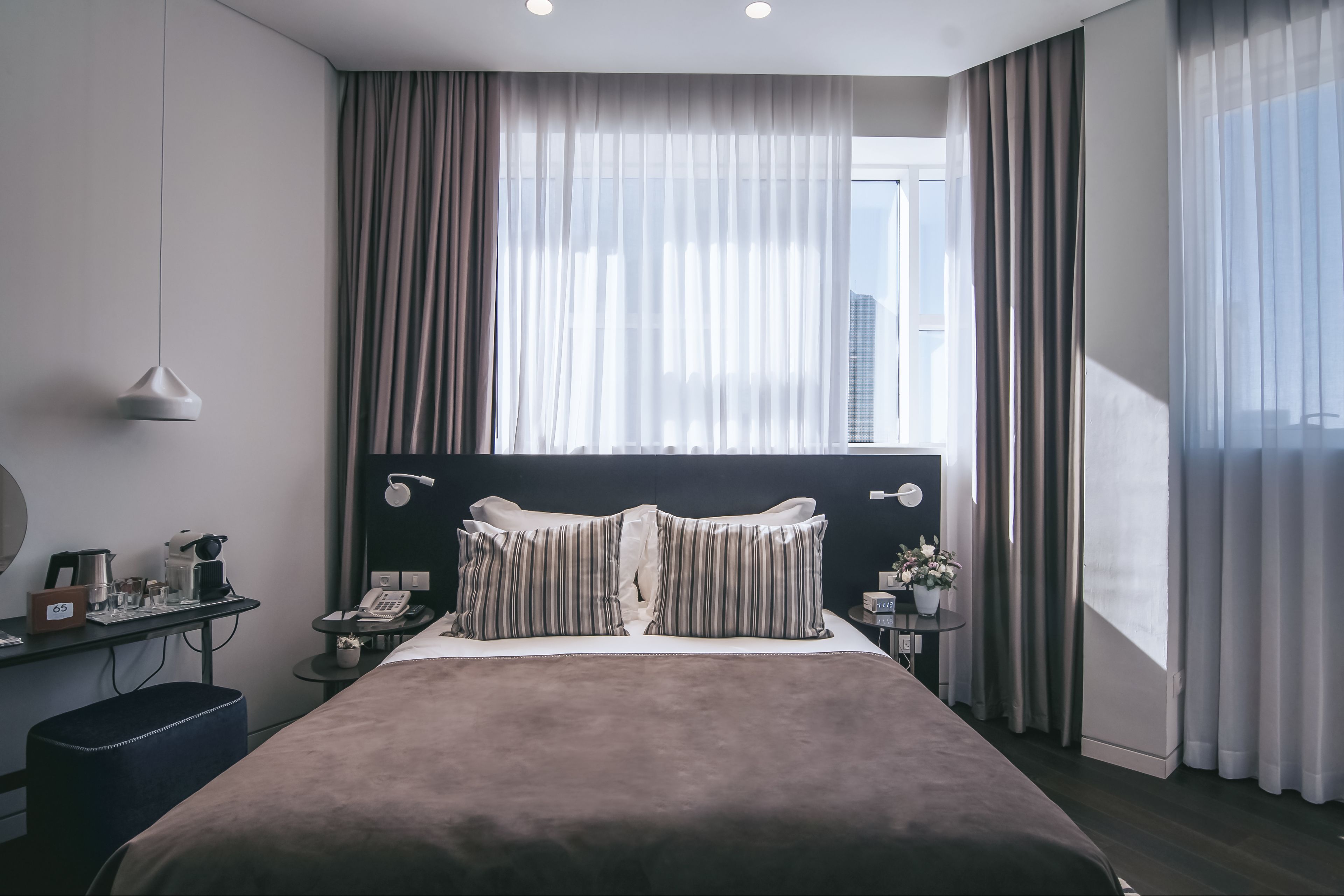 Una habitación de hotel moderna con una cama grande, una mesita de noche con lámpara, un teléfono y una pequeña mesa con una planta.