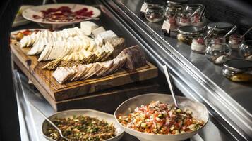 A buffet with various food items including sliced meats, cheeses, and a bowl of chopped vegetables.