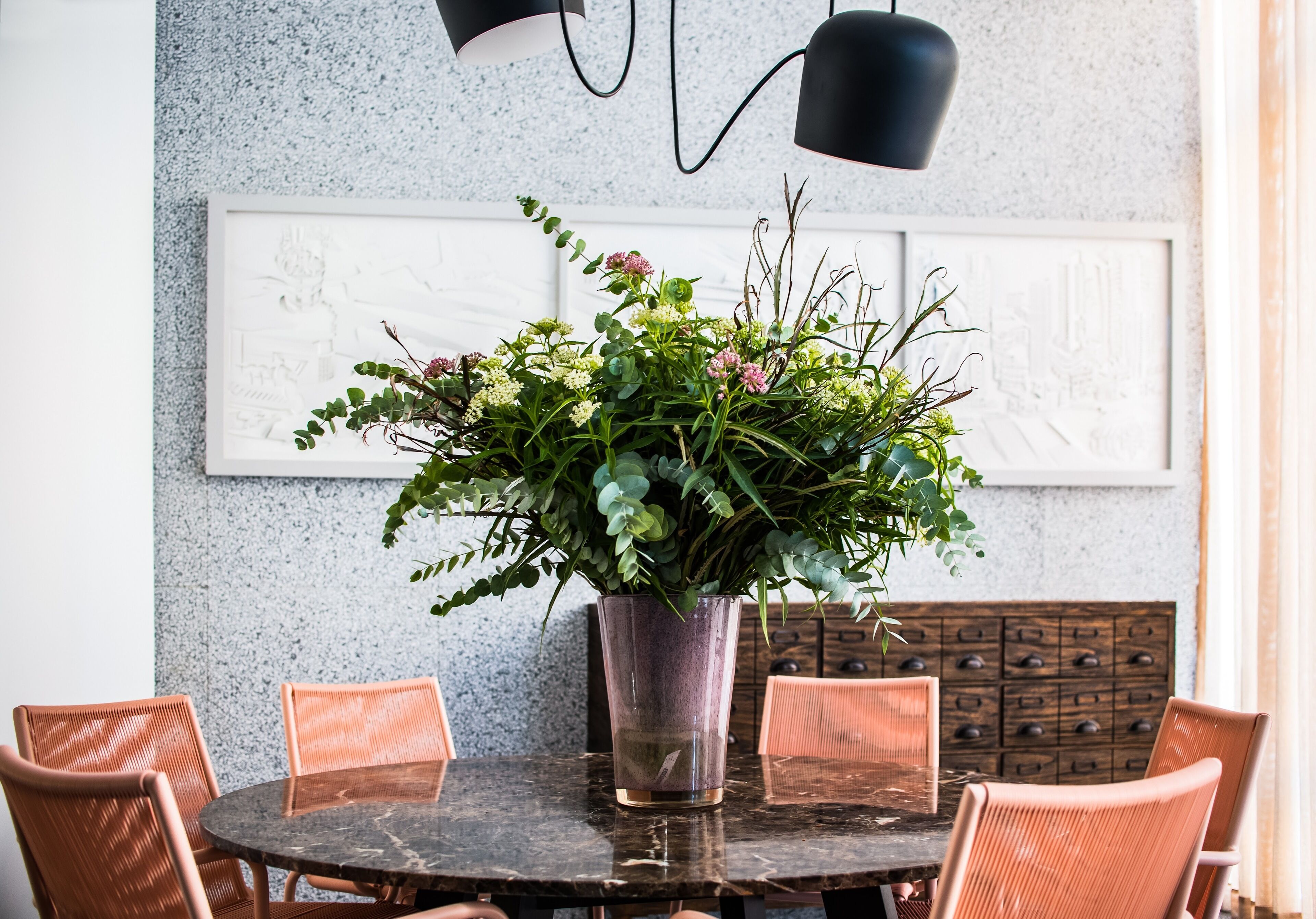 Une table ronde, ornée d’un pot de fleurs au centre, entourée de chaises en osier.