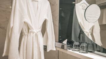A bathroom with a white robe hanging on a rack, a mirror, and a shelf with glass jars.