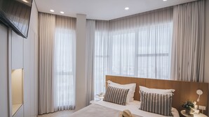 A modern hotel room with a large bed, two bedside tables, a TV mounted on the wall, and large windows with sheer curtains. - 65 Hotel, Rothschild Tel Aviv - an Atlas Boutique Hotel (Tel Aviv)