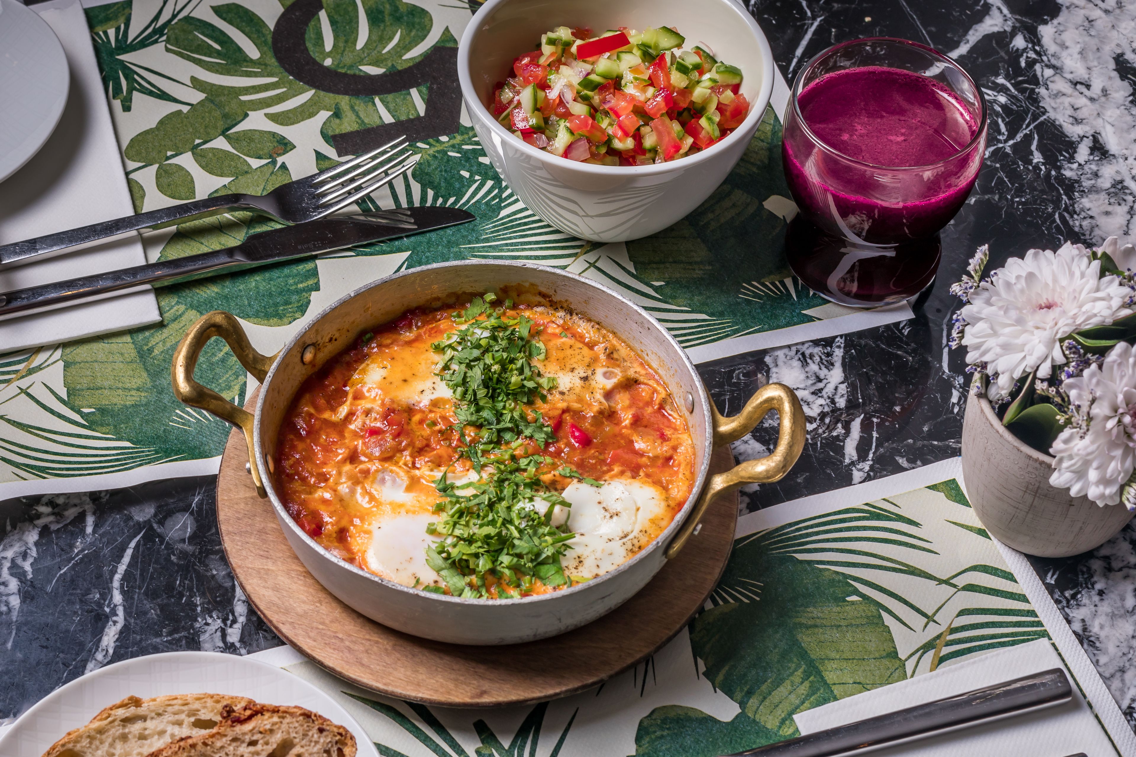 Una mesa de comedor con un plato de comida, un vaso de bebida y una fuente de pan.